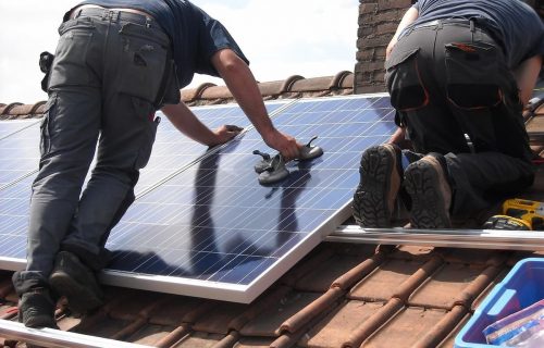 Deux techniciens en train de poser un panneau solaire sur une toiture de maison - installation photovoltaïque en cours